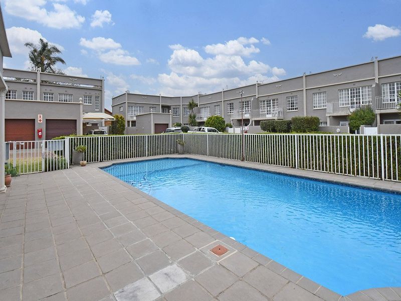A communal swimming pool area featuring a paved deck and secure metal fencing, set within a well-maintained apartment complex.