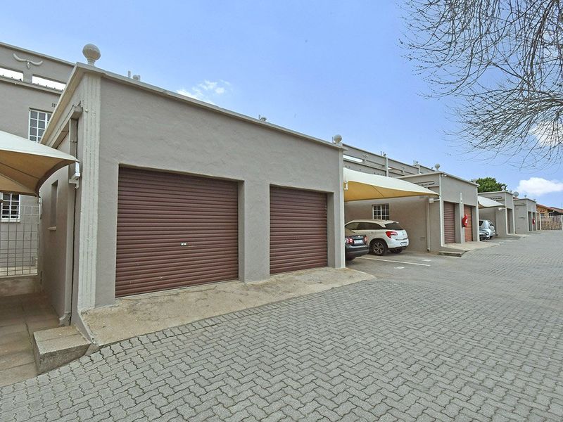 A row of apartment garages featuring roller shutter doors and adjacent paved parking bays with shade sail coverings.