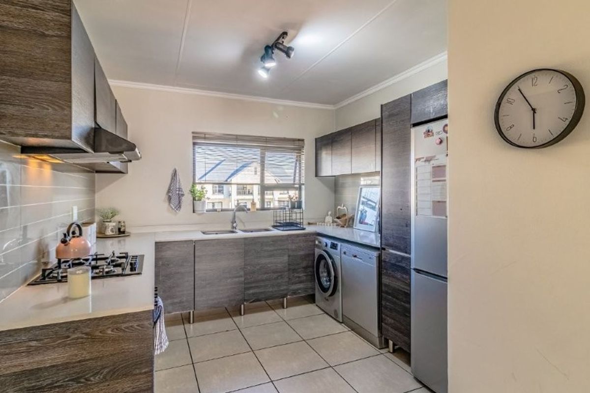 Modern kitchen featuring dark wood-grain cabinetry, stone-look countertops, gas hob, extractor fan, and integrated space for laundry appliances.