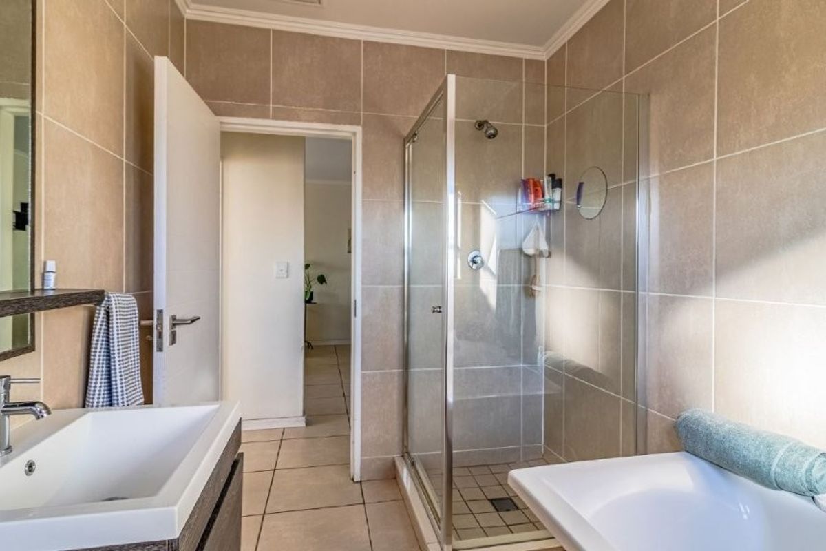 Modern bathroom featuring a glass-enclosed shower, vanity basin with storage cabinet, and neutral wall and floor tiling.