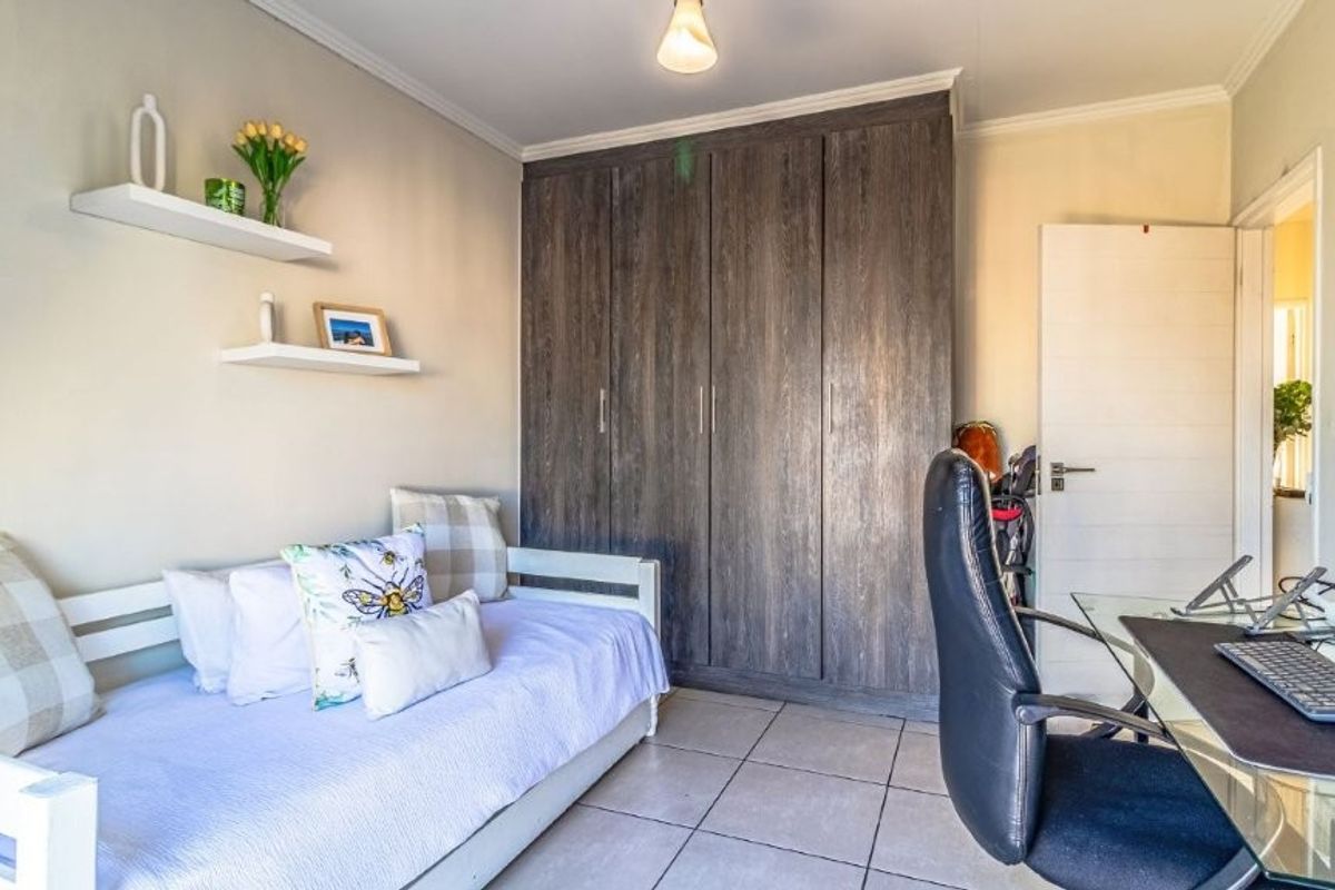 A functional bedroom featuring built-in cupboards, tiled flooring, and floating wall shelves, offering a practical layout for a bedroom or home office space.