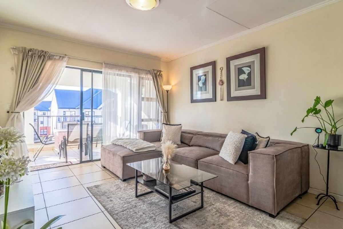 A bright and comfortable living room featuring tiled flooring and a large sliding glass door that opens onto a private balcony.