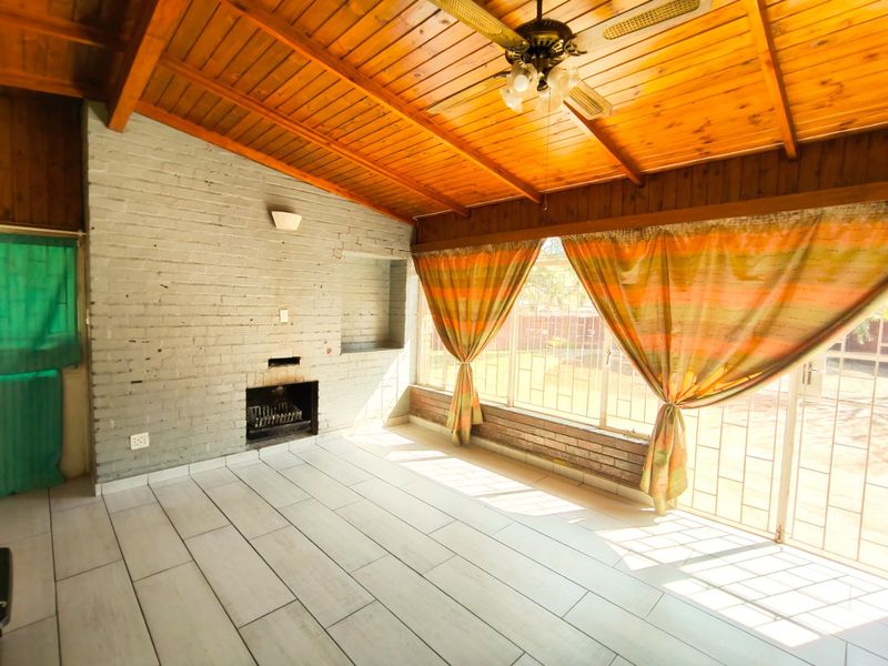 A spacious enclosed patio featuring a timber ceiling, tiled floors, and a built-in brick fireplace, offering a versatile space for outdoor living.