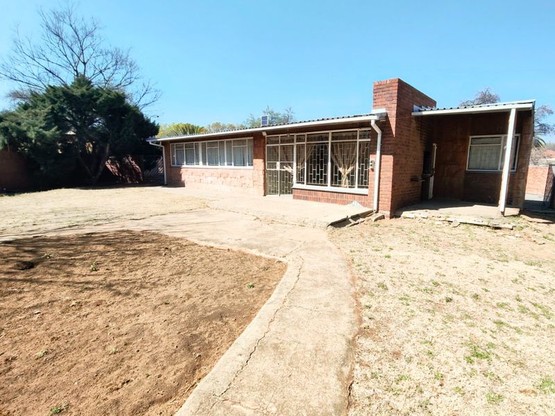 Rear view of a single-story brick house featuring a concrete patio, security-barred windows, and a large backyard area.