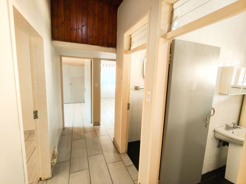 A functional hallway featuring tiled flooring and timber ceiling accents, providing access to adjacent rooms and a bathroom with a pedestal basin.