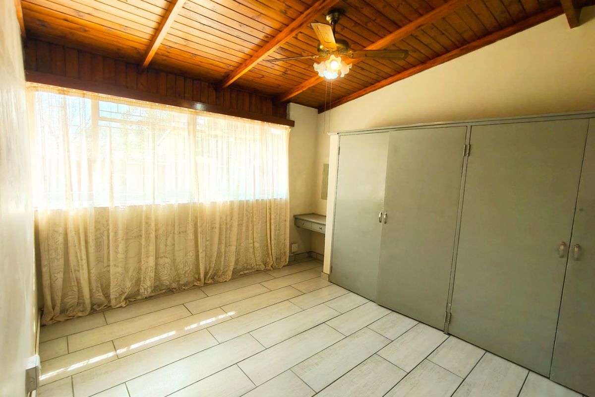 A spacious bedroom featuring tiled flooring, a wooden ceiling with a fan, and extensive built-in cupboards with an integrated vanity area.