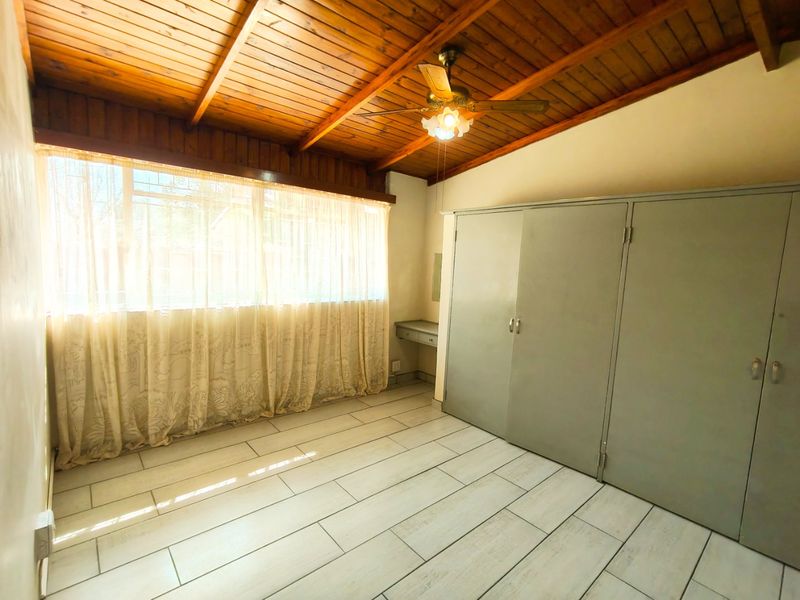 A spacious bedroom featuring tiled flooring, a wooden ceiling with a fan, and extensive built-in cupboards with an integrated vanity area.