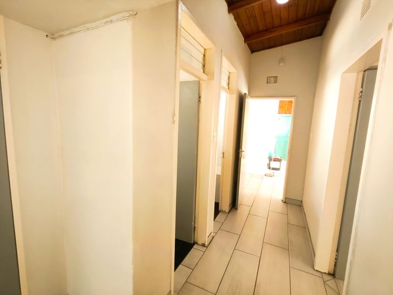 A bright, tiled hallway featuring an exposed timber ceiling and multiple internal doorways providing access to various rooms within the home.