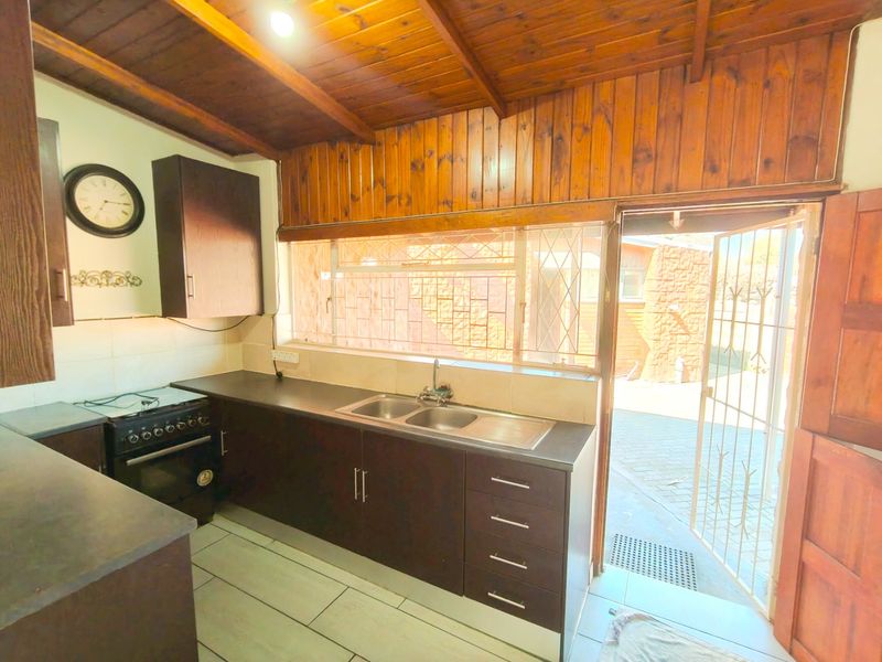 A functional kitchen featuring dark wood cabinetry, laminate countertops, a double bowl sink, and a timber-clad ceiling with direct access to the exterior.