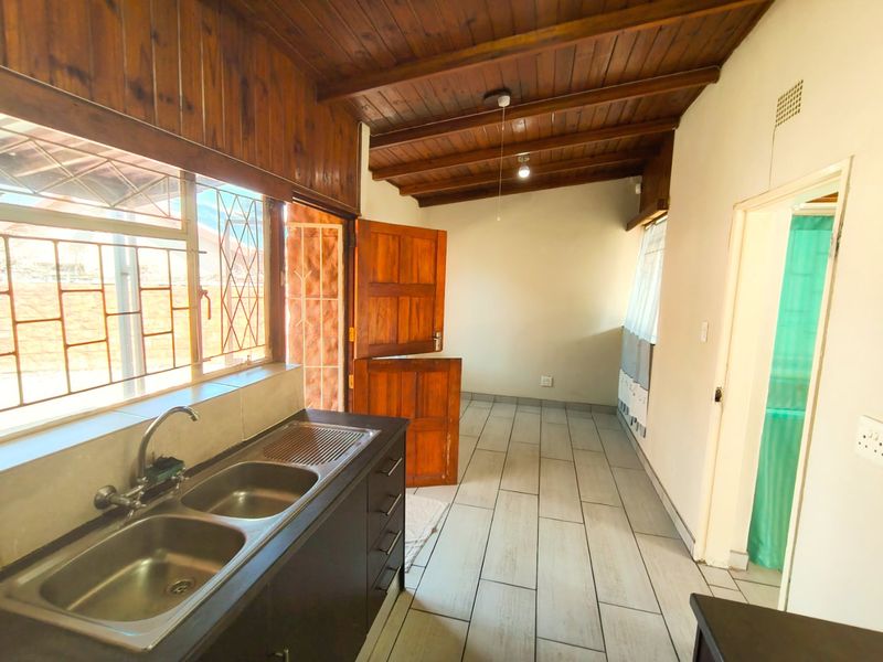 A functional scullery area featuring a double bowl sink, tiled flooring, and a distinctive exposed timber beam ceiling with a stable door exit.
