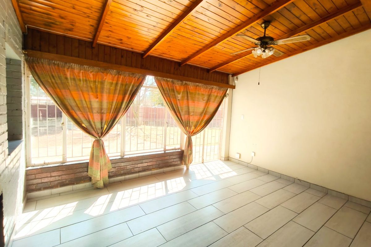 Spacious living area featuring a vaulted timber-clad ceiling, ceiling fan, and large windows with security bars, finished with neutral floor tiles.