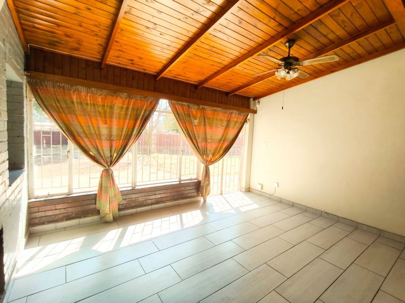 Spacious living area featuring a vaulted timber-clad ceiling, ceiling fan, and large windows with security bars, finished with neutral floor tiles.