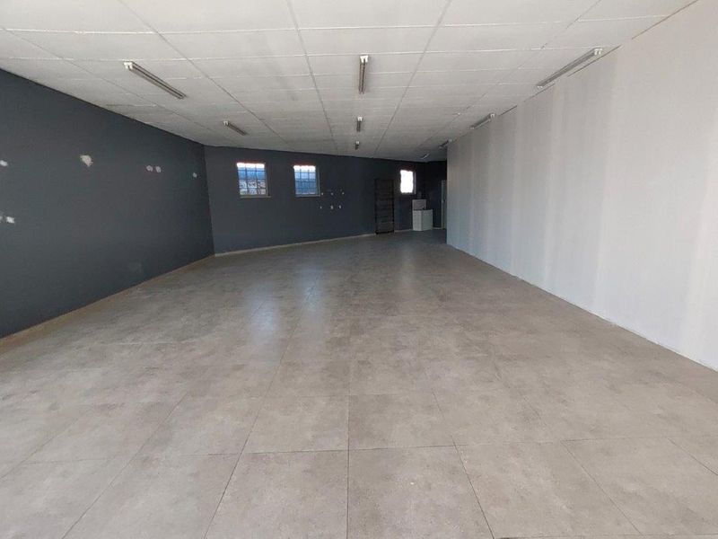 A spacious, vacant commercial open-plan area featuring large format floor tiles, a suspended ceiling with integrated lighting, and dark accent walls.
