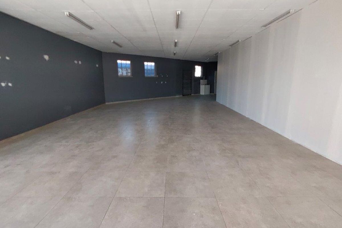 A spacious, vacant open-plan commercial area featuring large format floor tiles, a suspended ceiling with integrated lighting, and neutral wall finishes.