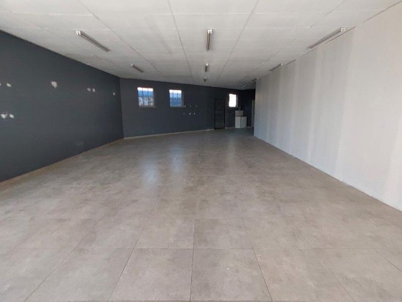 A spacious, vacant open-plan commercial area featuring large format floor tiles, a suspended ceiling with integrated lighting, and neutral wall finishes.
