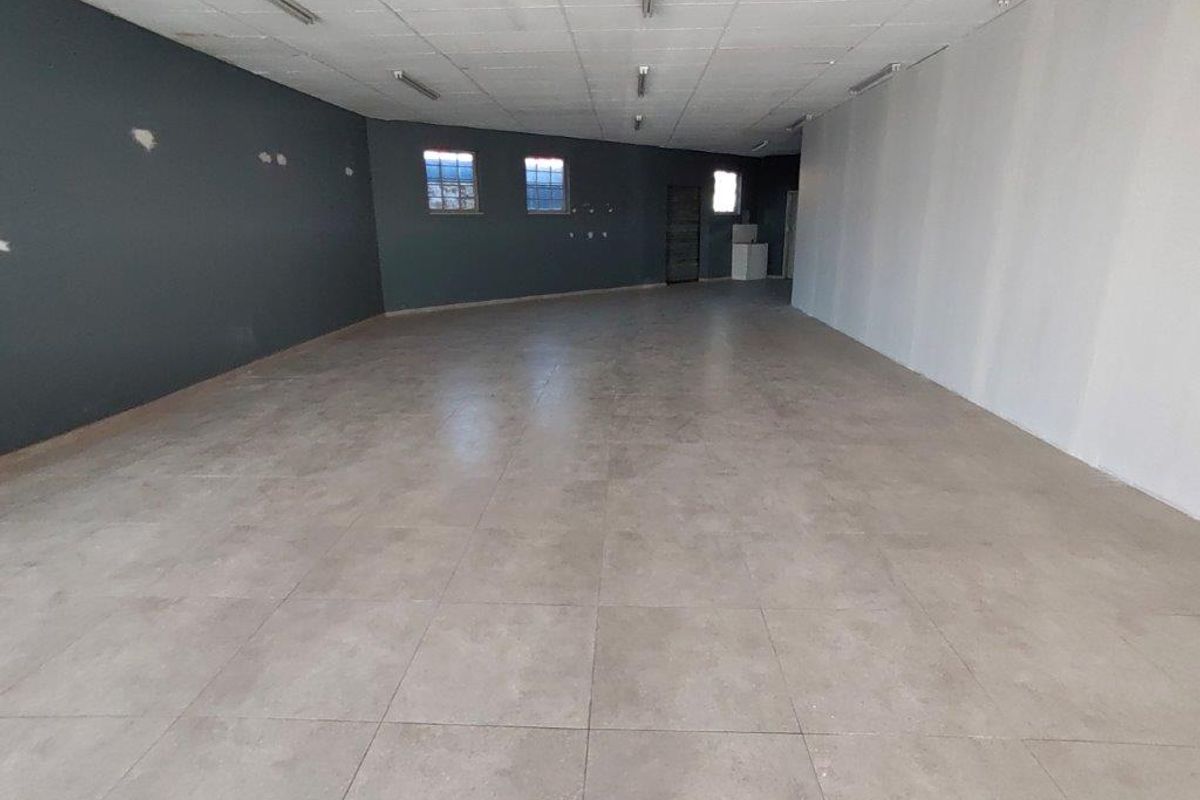 A spacious, empty commercial open-plan area featuring tiled flooring, suspended ceiling lighting, and dual-tone painted walls, suitable for various business configurations.