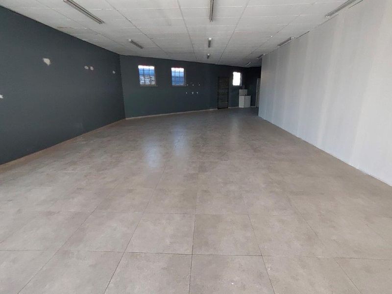 A spacious, empty commercial open-plan area featuring tiled flooring, suspended ceiling lighting, and dual-tone painted walls, suitable for various business configurations.