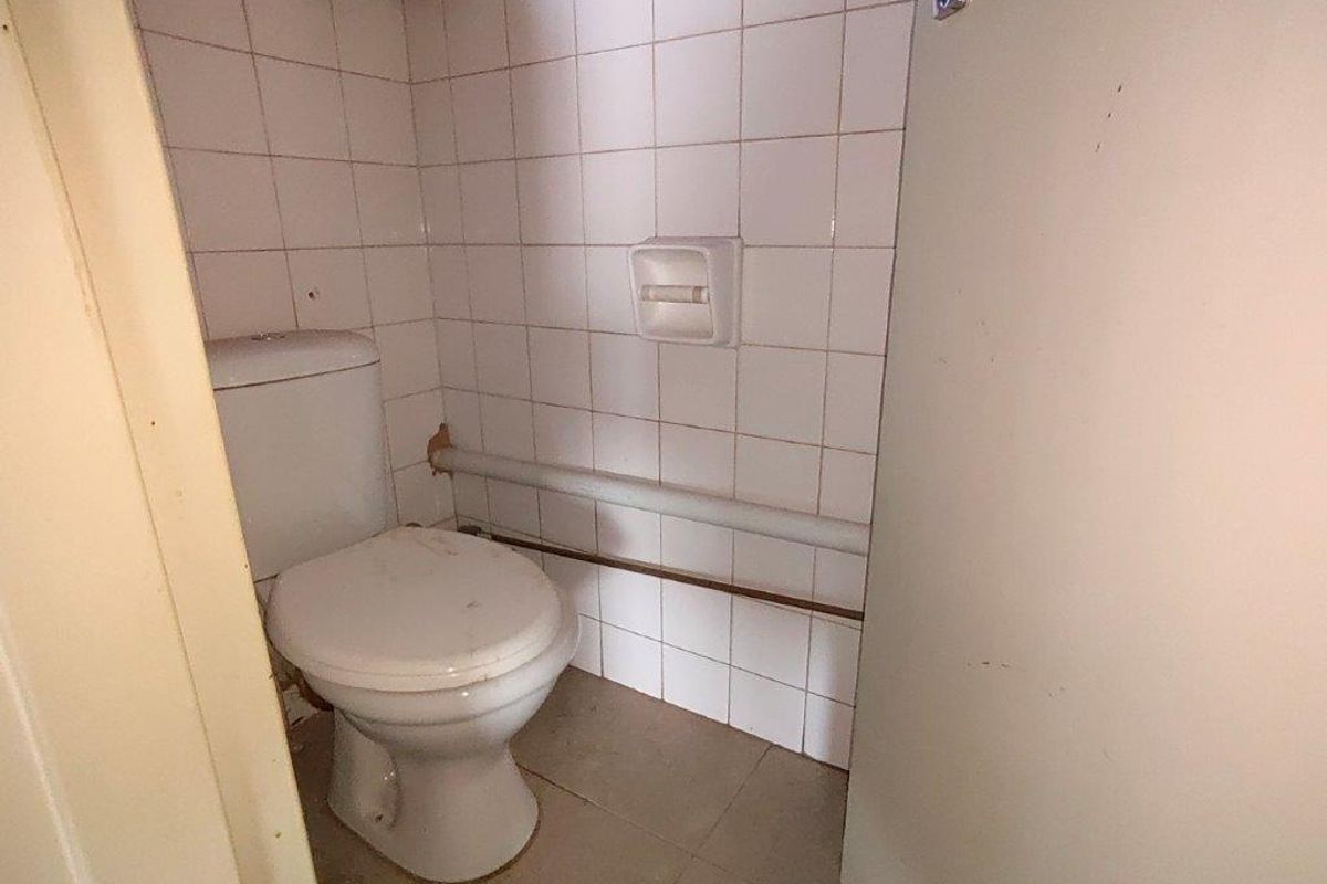 A small, dated bathroom featuring a standard toilet, tiled walls, and exposed plumbing, requiring cosmetic updates and maintenance.