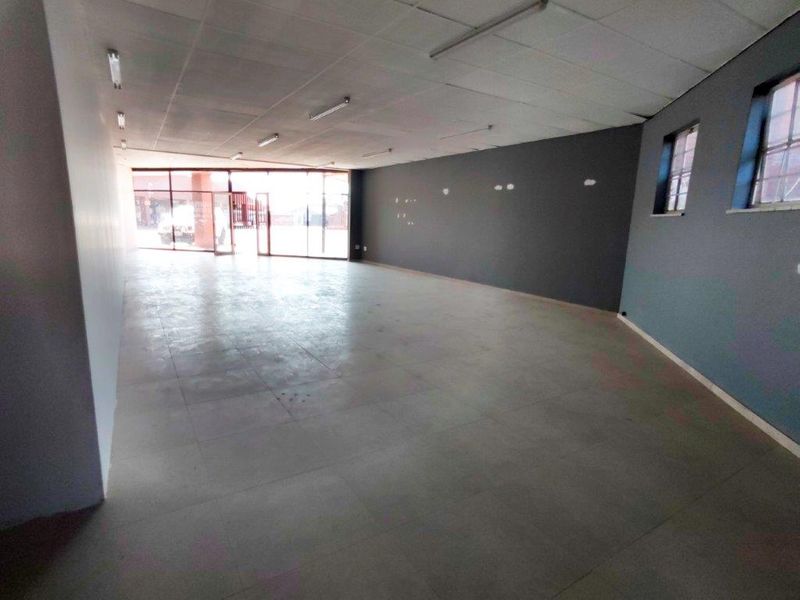 A spacious, vacant commercial open-plan unit featuring tiled flooring, a suspended ceiling, and a large glass storefront providing ample natural light.