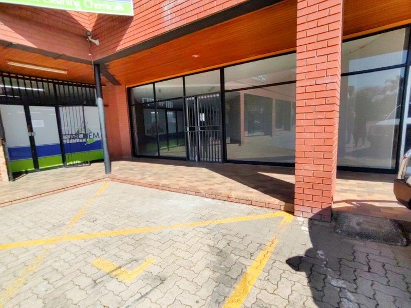 Commercial storefront featuring a brick facade, large glass display windows, security gate, and a paved parking area in front.
