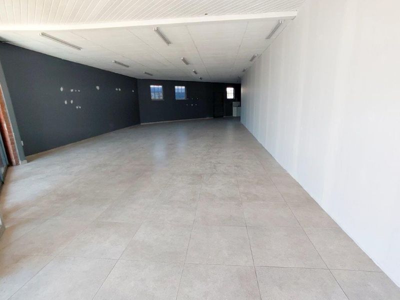 A spacious, empty commercial open-plan area featuring tiled flooring, a suspended ceiling with integrated lighting, and neutral wall finishes.