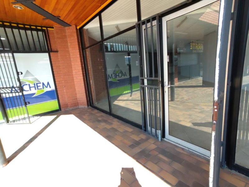 Commercial storefront entrance featuring a glass facade, security gate, and tiled walkway under a timber-lined covered entryway.