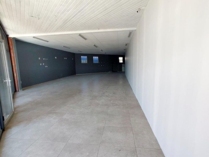 A spacious, empty commercial open-plan area featuring tiled flooring, a timber panel ceiling, and neutral wall finishes, suitable for various business configurations.
