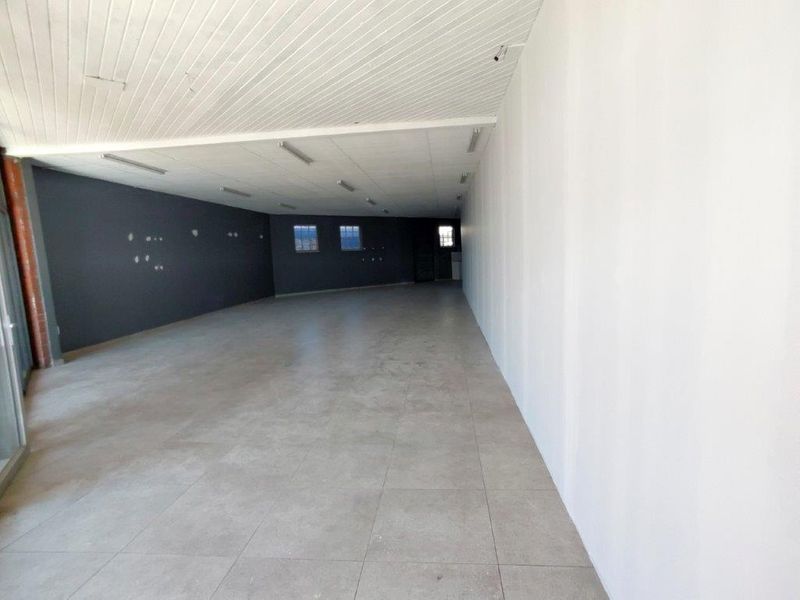 A spacious, empty open-plan commercial unit featuring tiled flooring, recessed lighting, and a neutral color palette, suitable for various business applications.