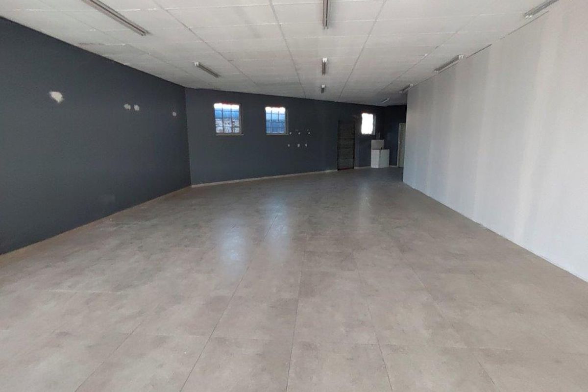 A spacious, empty commercial open-plan area featuring tiled flooring, a suspended ceiling with fluorescent lighting, and dark accent walls.