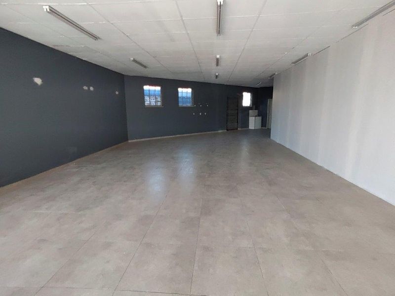 A spacious, empty commercial open-plan area featuring tiled flooring, a suspended ceiling with fluorescent lighting, and dark accent walls.