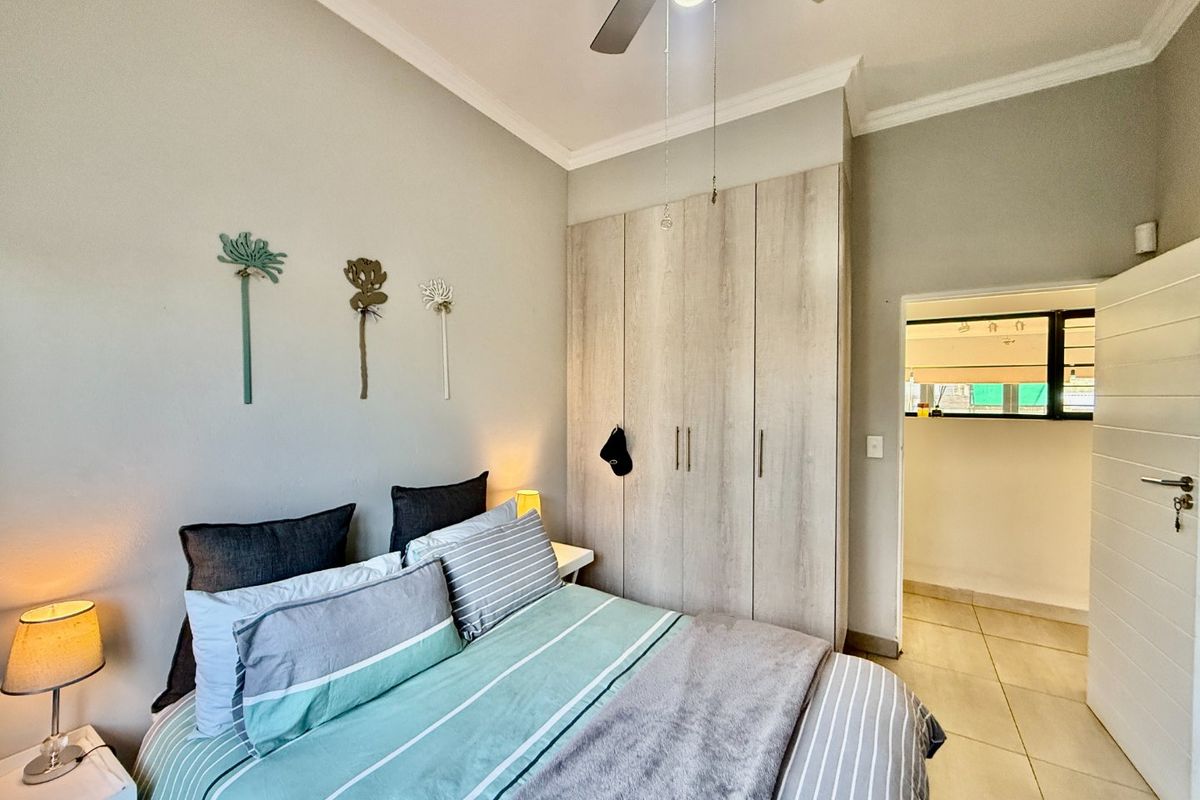 A well-maintained bedroom featuring built-in cupboards, a ceiling fan, and neutral tiled flooring, with an adjacent doorway leading to an adjoining space.