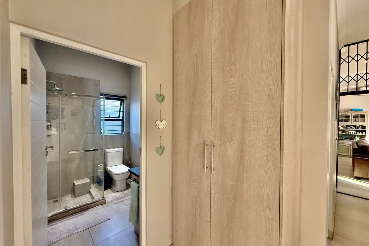 A modern bathroom featuring a glass-enclosed shower, toilet, and adjacent built-in wooden cupboards in the hallway area.