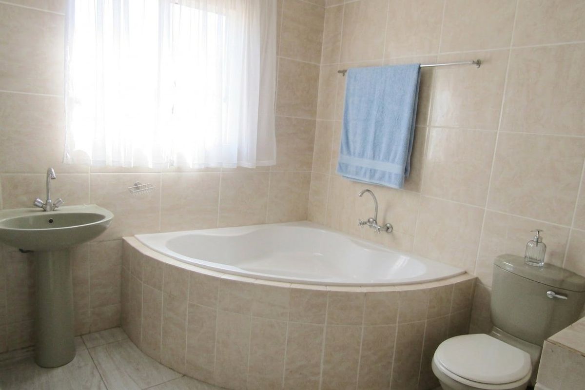 A functional bathroom featuring a corner bathtub, pedestal basin, and toilet with neutral wall and floor tiling.