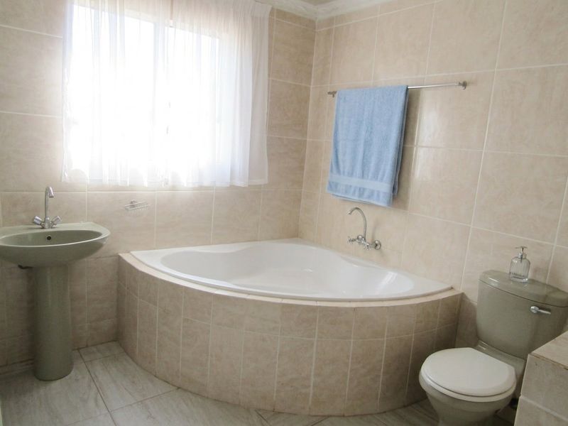 A functional bathroom featuring a corner bathtub, pedestal basin, and toilet with neutral wall and floor tiling.