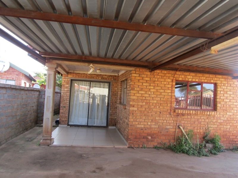 Covered patio area featuring a corrugated metal roof, brick exterior walls, and a sliding glass door entrance.