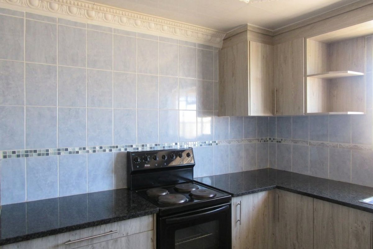 A functional kitchen featuring light wood-look cabinetry, dark granite countertops, and a blue tiled backsplash with decorative mosaic accents.