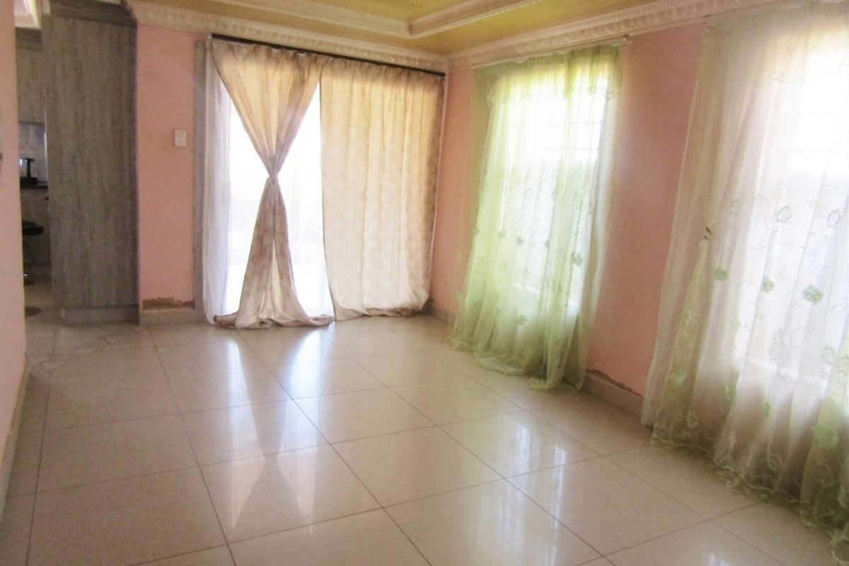 An empty living room featuring tiled flooring, a recessed ceiling, and large windows with sliding glass door access to the exterior.