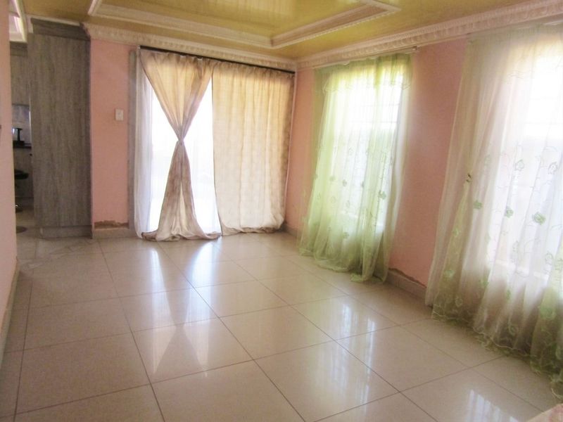 An empty living room featuring tiled flooring, a recessed ceiling, and large windows with sliding glass door access to the exterior.