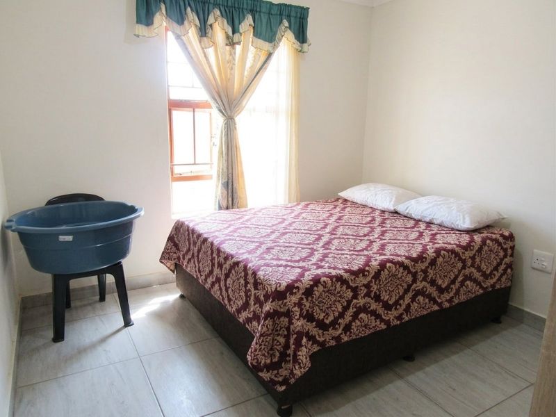 A simple bedroom featuring tiled flooring and a window, providing a functional space for rest.