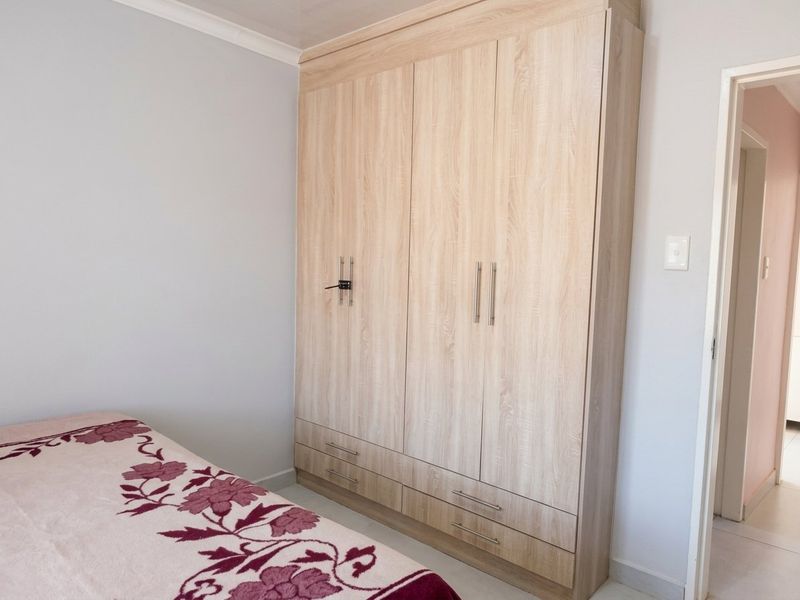 A bedroom featuring a modern light wood-finish built-in wardrobe with integrated drawers and sleek metal handles.