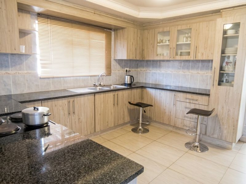 A well-maintained kitchen featuring light wood-look cabinetry, dark granite countertops, ceramic tile flooring, and a built-in glass display cabinet.