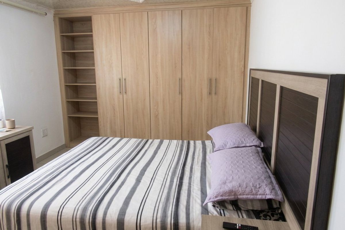 A well-maintained bedroom featuring extensive light wood-grain built-in cupboards with integrated shelving and decorative coved ceiling detailing.