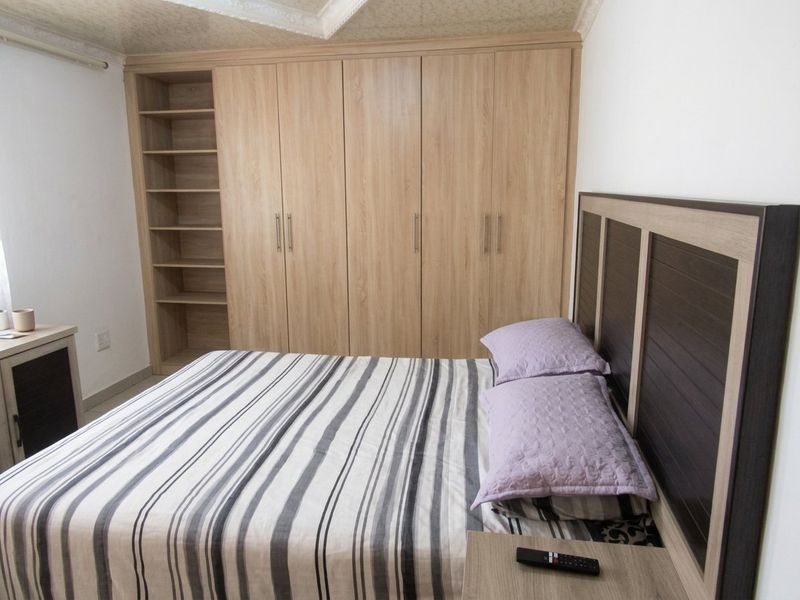 A well-maintained bedroom featuring extensive light wood-grain built-in cupboards with integrated shelving and decorative coved ceiling detailing.