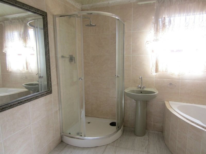 A functional bathroom featuring a corner bathtub, a separate shower enclosure, and a pedestal basin with neutral wall and floor tiling.