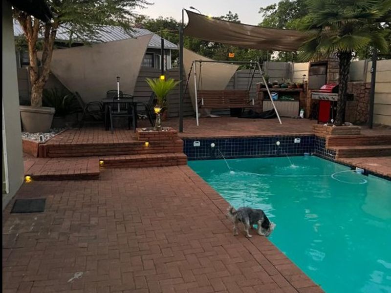 Outdoor entertainment area featuring a swimming pool with water features, brick paved patio, built-in braai, and shade sails for comfortable outdoor living.
