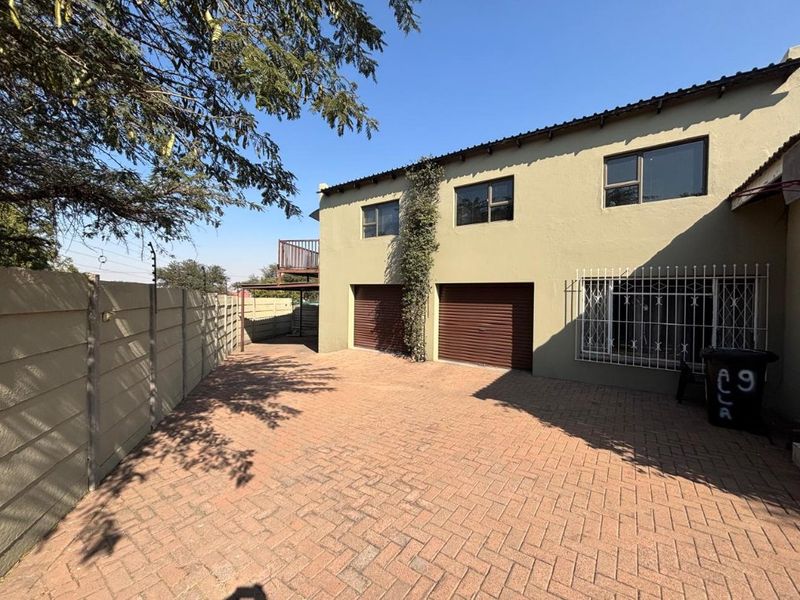 Front exterior view featuring a paved driveway, double garage, and secure boundary walling with electric fencing.