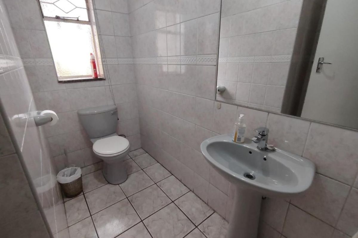 A functional bathroom featuring a pedestal basin, toilet, and neutral wall and floor tiling with a fixed mirror.