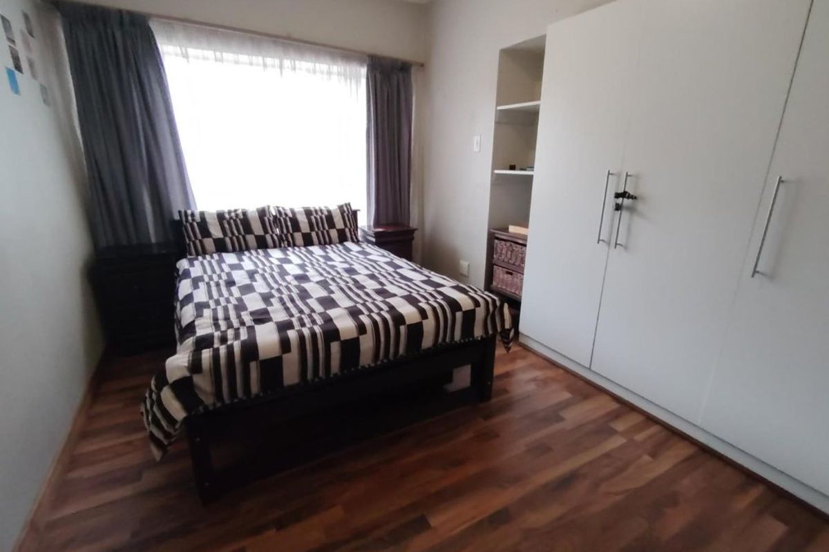 A functional bedroom featuring laminate flooring, a large window with curtains, and a built-in wardrobe with integrated shelving.