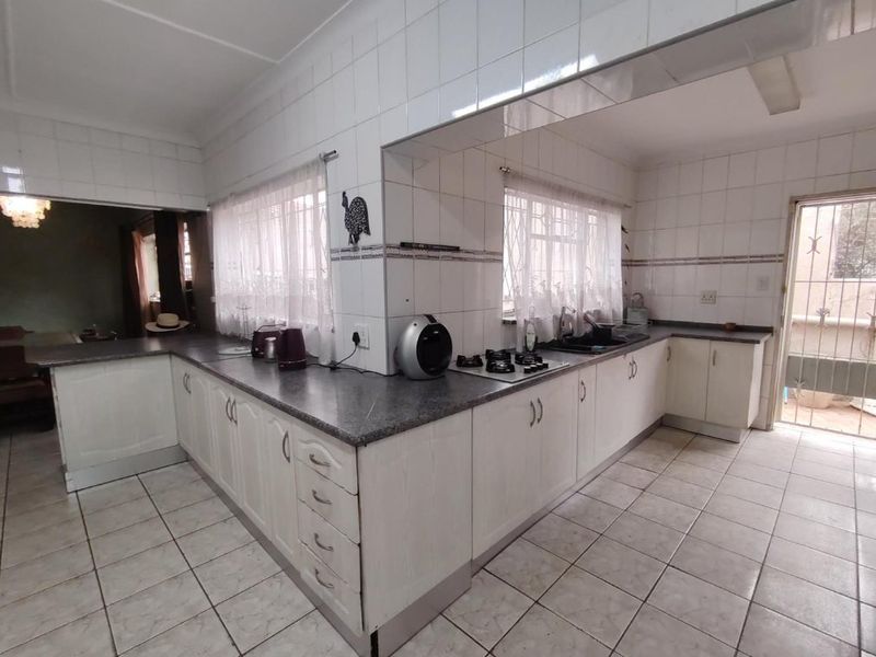 A functional kitchen featuring white cabinetry, dark laminate countertops, a gas hob, and tiled flooring with direct access to an outdoor area.
