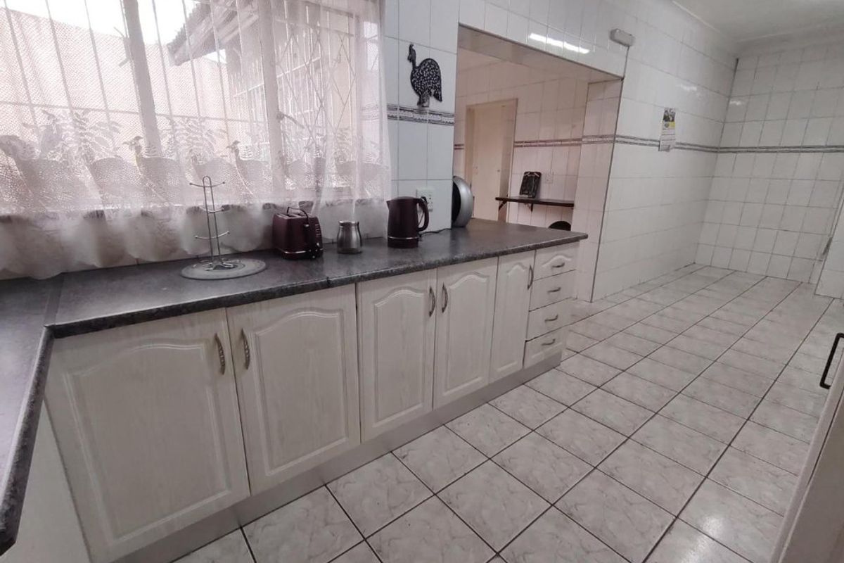 A functional kitchen featuring white cabinetry, laminate countertops, and fully tiled walls and floors, with an adjacent scullery or utility area.